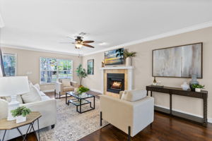 Bright living room featuring engineered wood floors, crown molding, and cozy fireplace with stone surround.