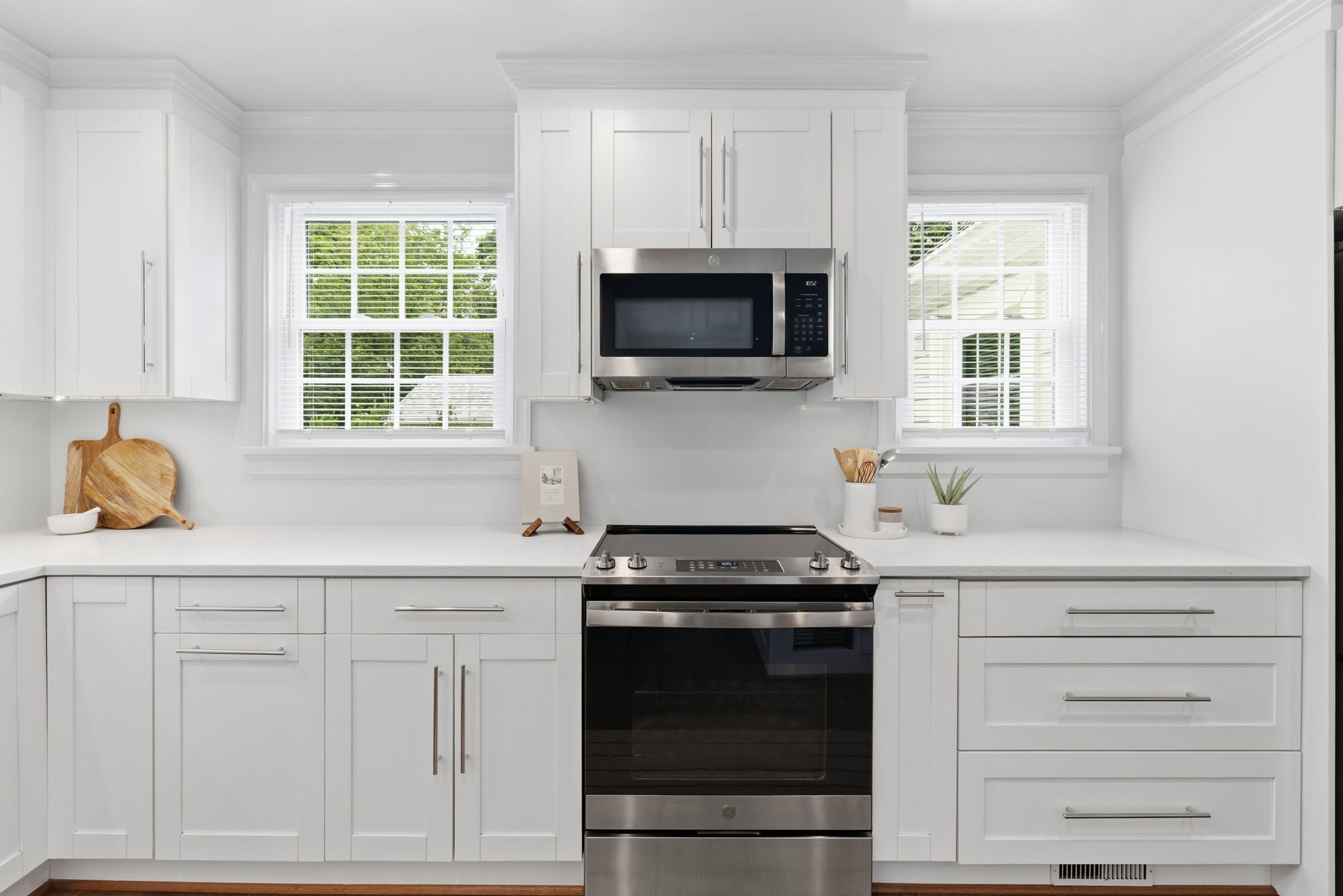 White shaker-style cabinetry with chrome hardware, white Quartz countertops, and stainless steel appliances. Counter space is often at a premium in these Cape Cod houses but not here!