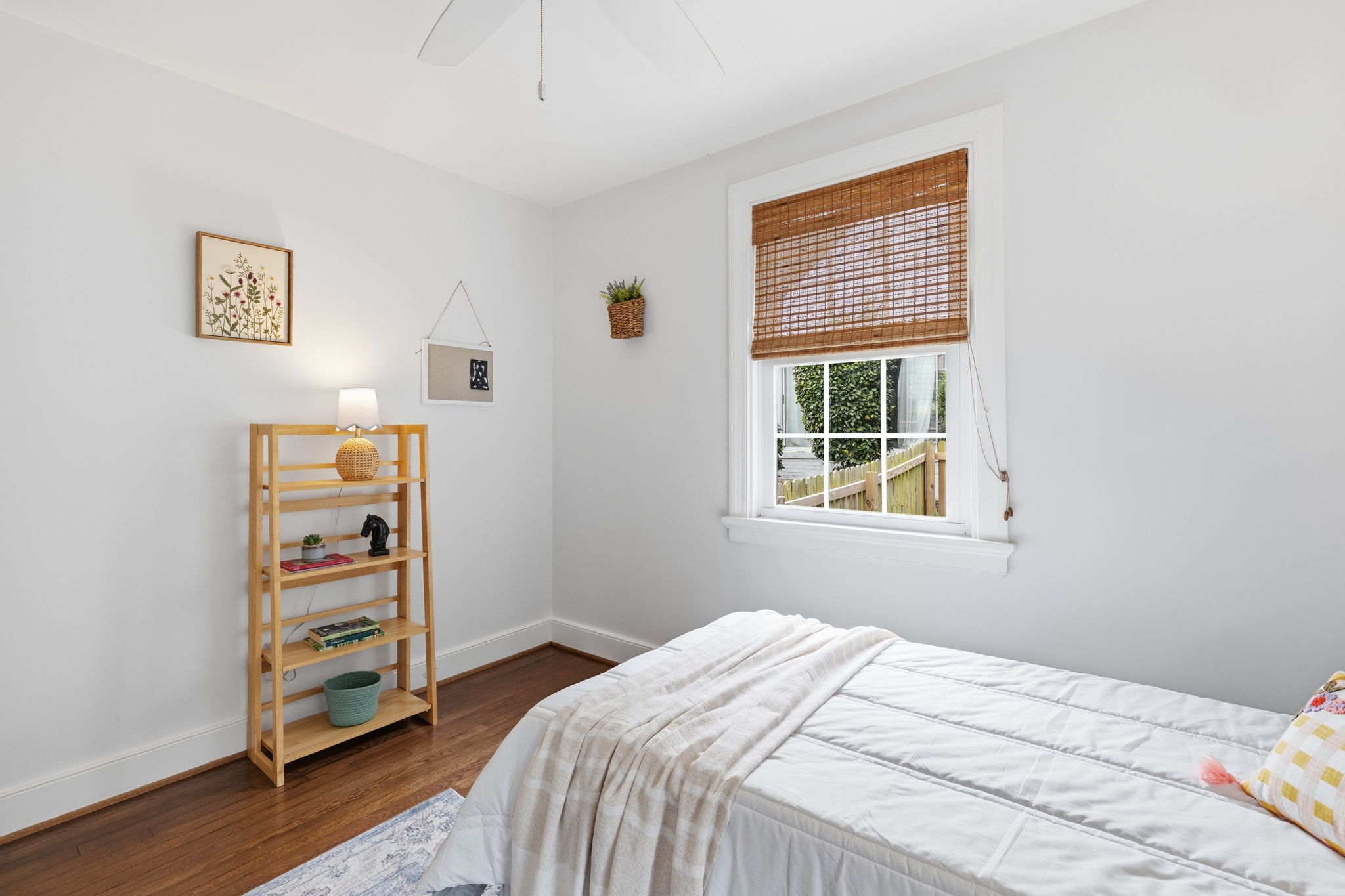 Hardwood flooring, crisp white walls, white window trim, natural fiber window treatment, and a ceiling fan.