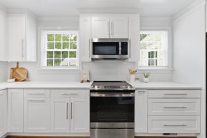 White shaker-style cabinetry with chrome hardware, white Quartz countertops, and stainless steel appliances. Counter space is often at a premium in these Cape Cod houses but not here!