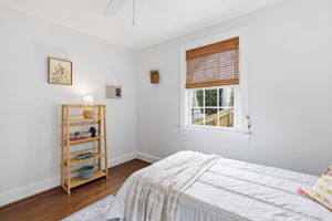 Hardwood flooring, crisp white walls, white window trim, natural fiber window treatment, and a ceiling fan.