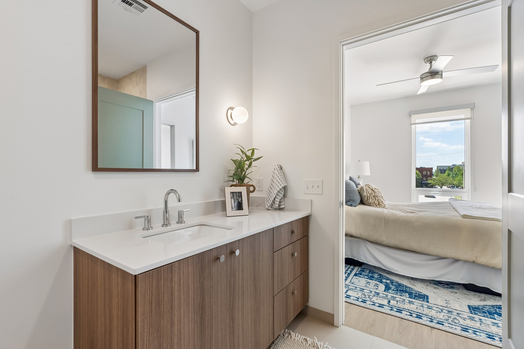 Model unit bathroom with a wood vanity, round mirror and quartz counter