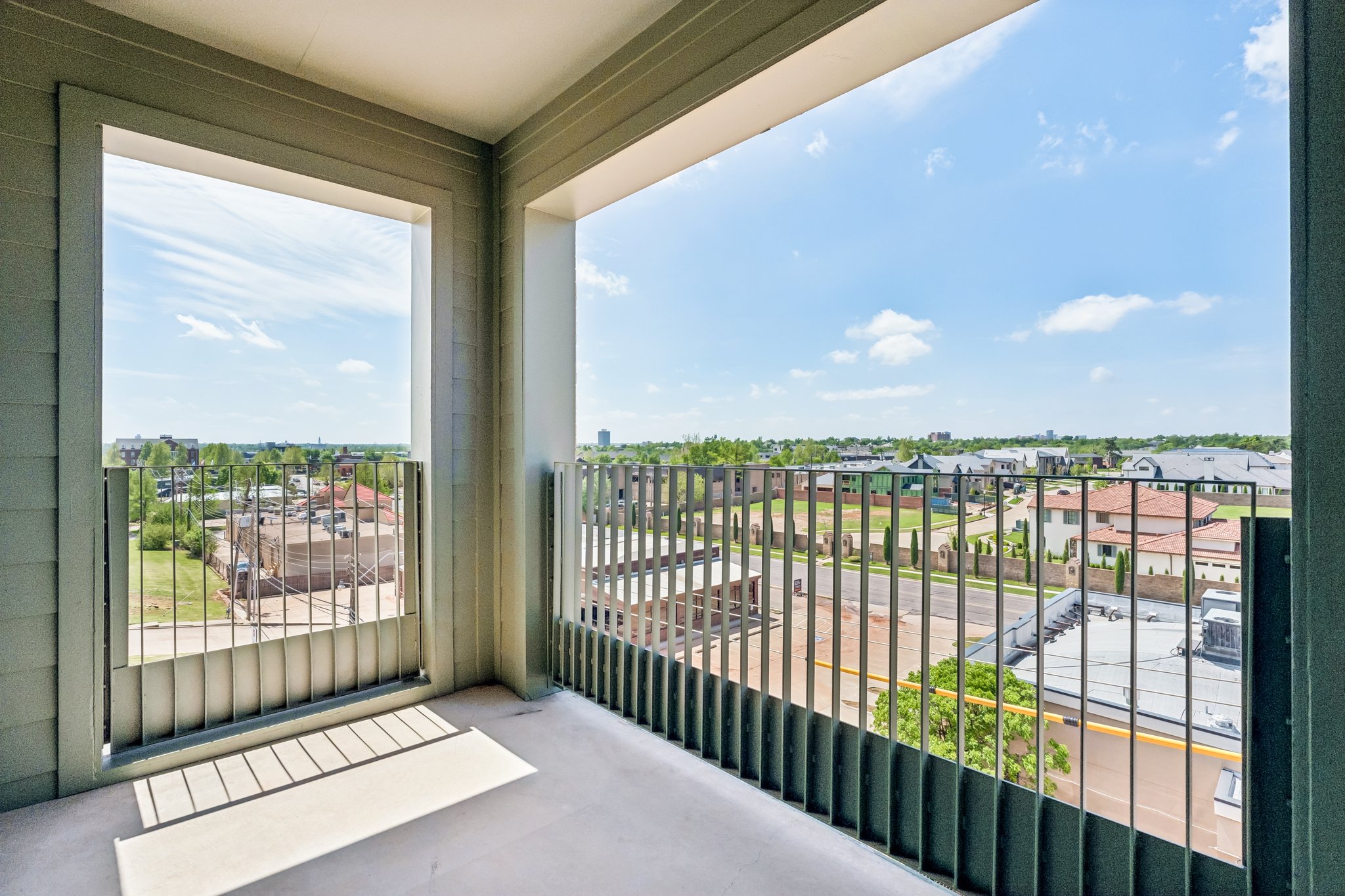 Covered unit balcony with a metal railing and a wide neighborhood view