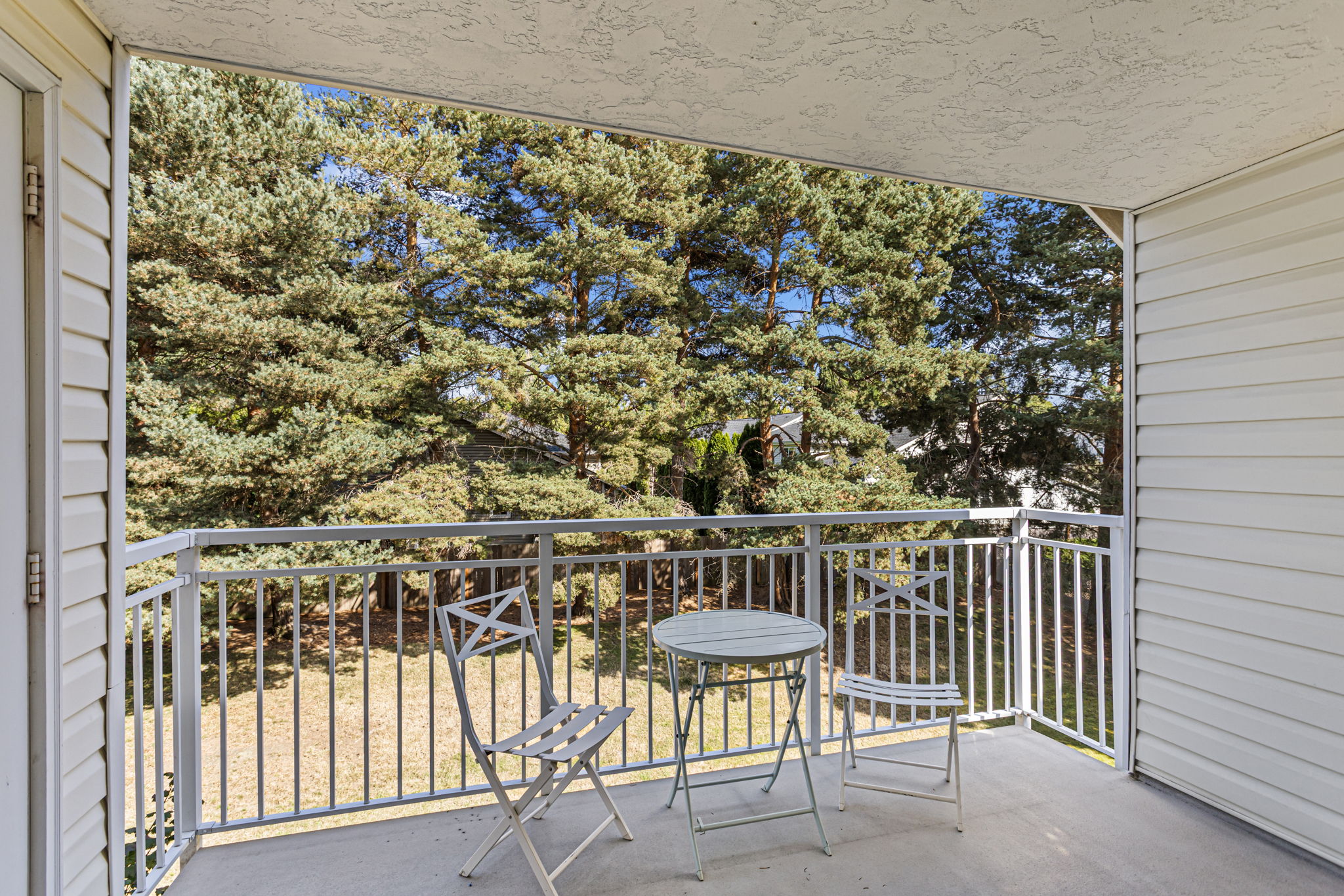 Photographer floor plan measures the covered balcony at approx. 91 sq. ft.—large enough to function as an outdoor room, with lawn and mature trees opening beyond the railing.