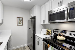 Unused since renovation, the kitchen pairs new white shaker cabinetry and quartz counters with a new stainless microwave and dishwasher.