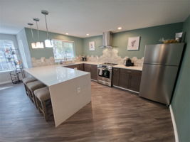 The clubhouse kitchen is spacious and like-new, with quartz counters, stainless appliances, and an open pass-through to the adjoining dining and living area.