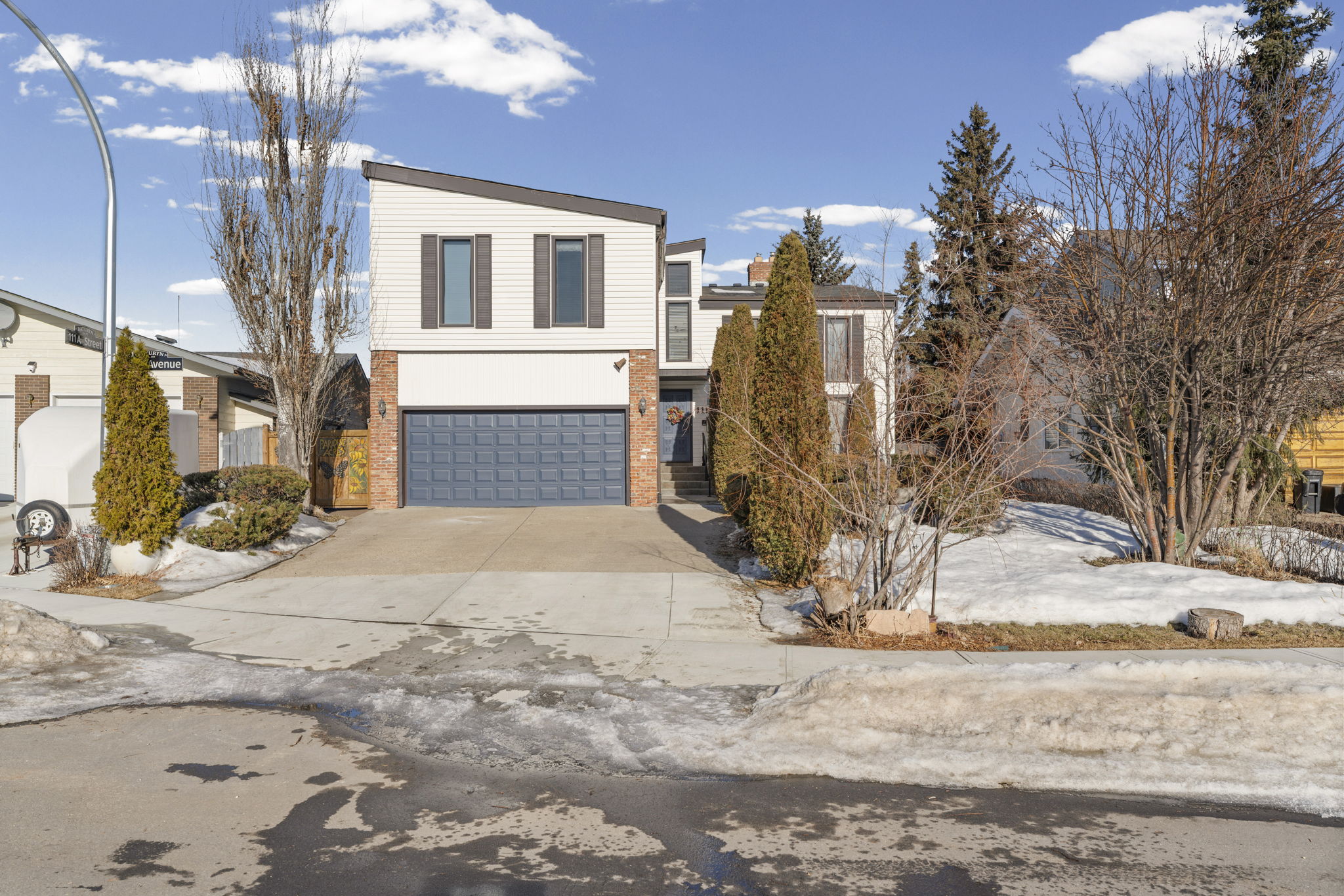 Daytime front view of the 173a Avenue home with a blue garage door and tall shrubs.