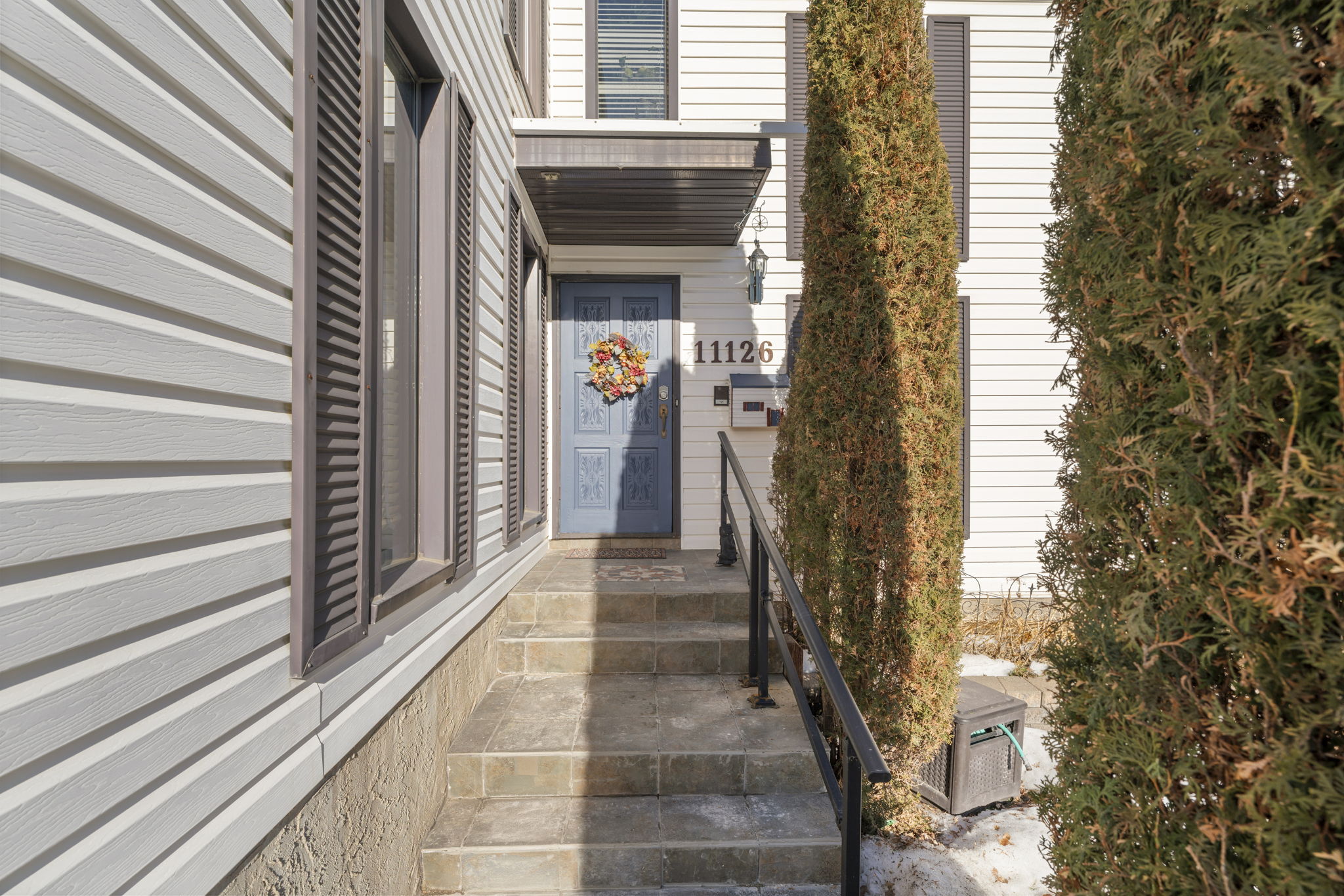 Narrow entrance path beside tall shrubs leading to a blue front door.