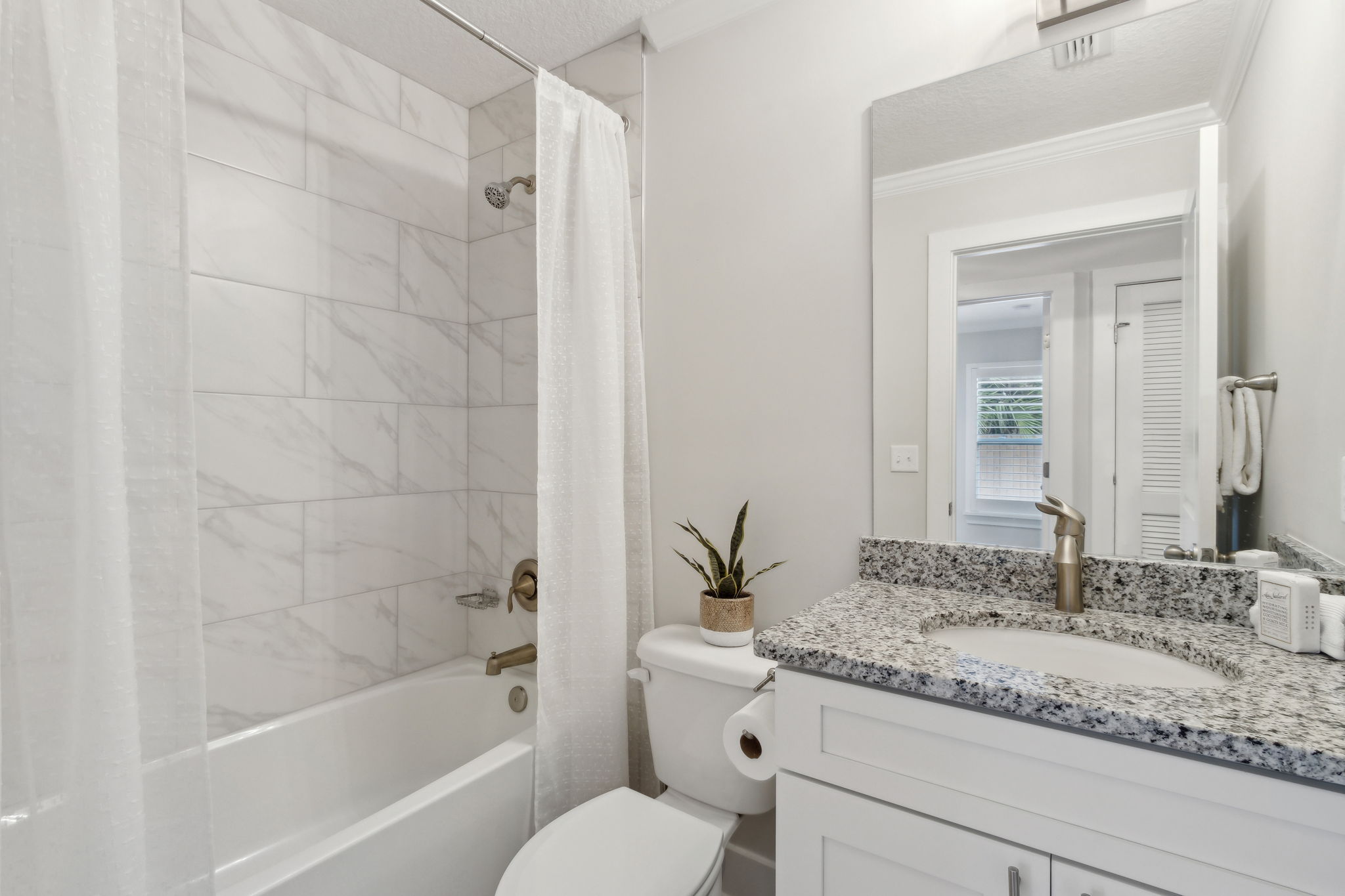 The modern guest bath offers granite vanity, sleek fixtures, and a tiled tub/shower combo.