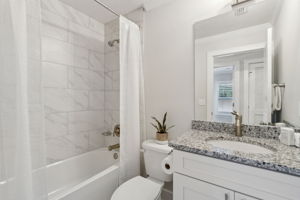The modern guest bath offers granite vanity, sleek fixtures, and a tiled tub/shower combo.