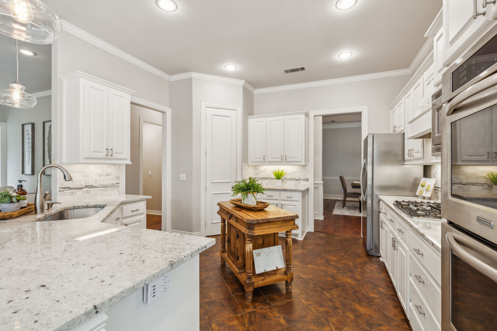 The kitchen includes a single-basin sink, under cabinet lighting, pendant lights above the breakfast bar, a walk-in pantry, and an island. NOTE: The refrigerator and kitchen island will remain with the home.