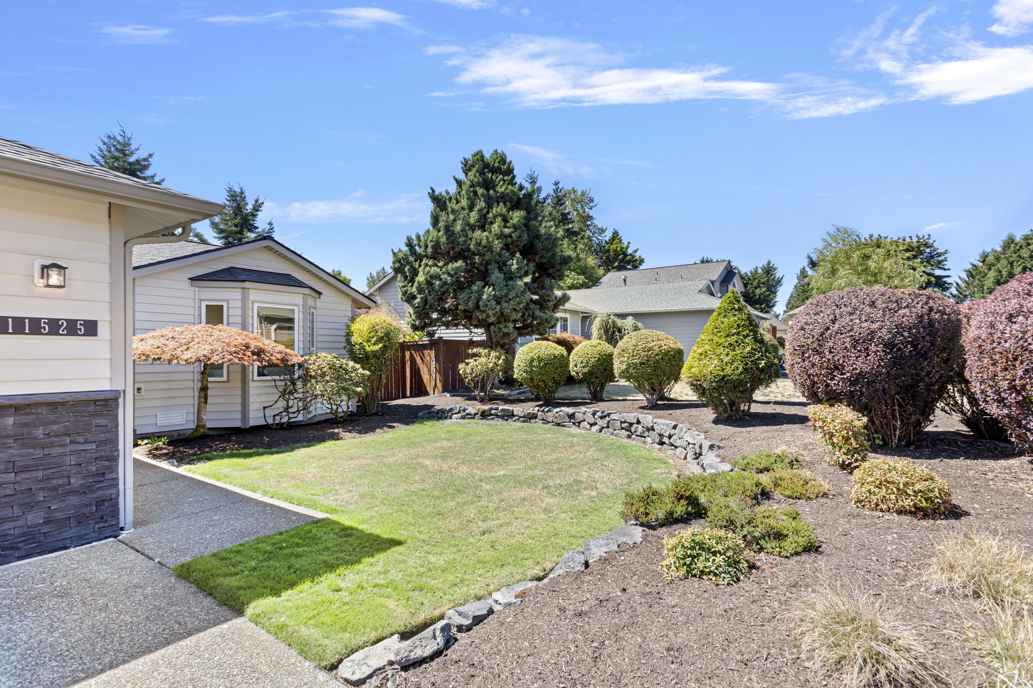 A wrap of mature plantings and rockery softens the yard’s edges, adding privacy, curb appeal, and year-round visual interest.