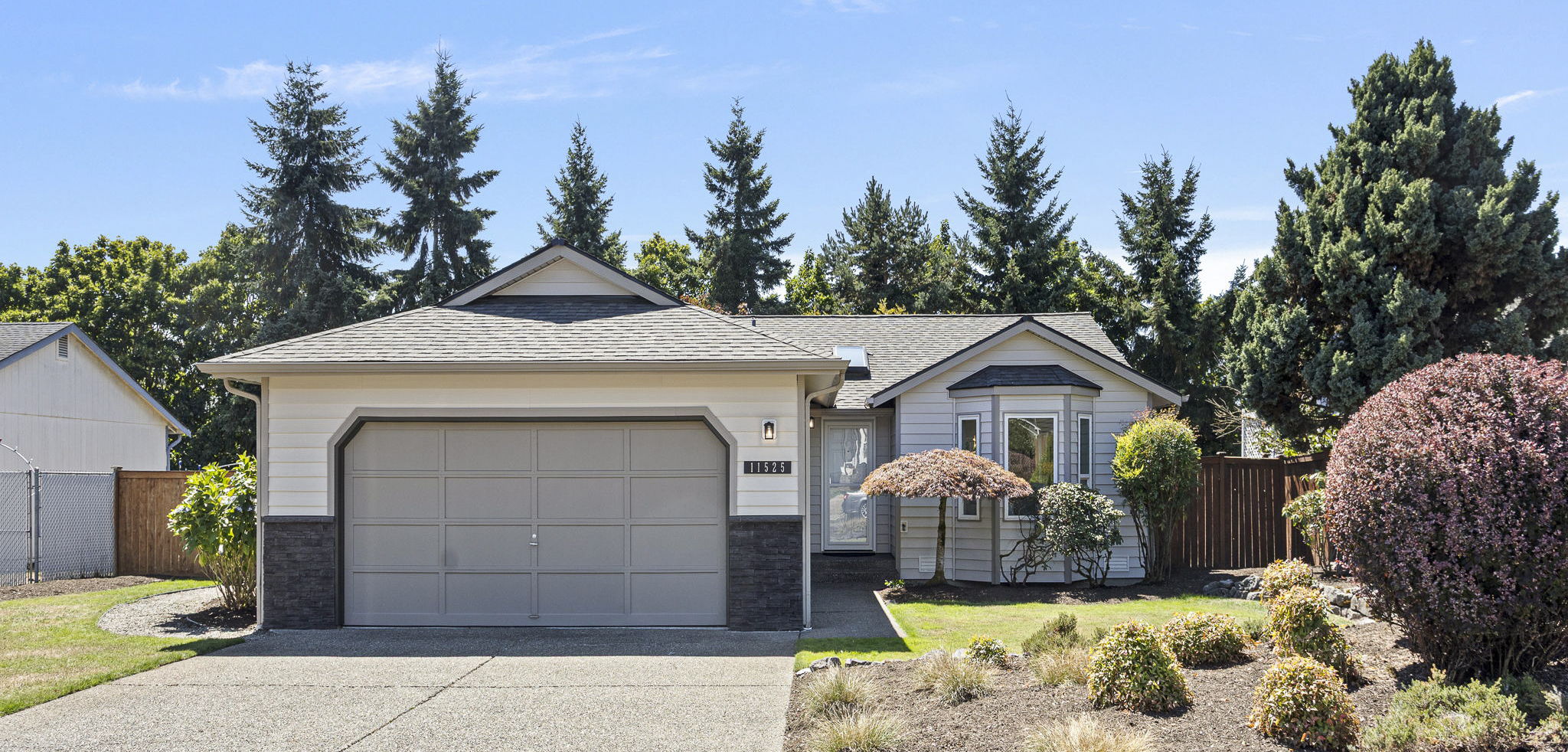 Wide front yard view showcasing mature plantings, fresh mulch, and the home’s inviting single-level design.