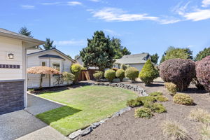 A wrap of mature plantings and rockery softens the yard’s edges, adding privacy, curb appeal, and year-round visual interest.