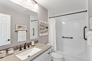 Freshly updated full bath with sleek quartz-look counters, bronze fixtures, and accessibility grab bars for ease and safety.