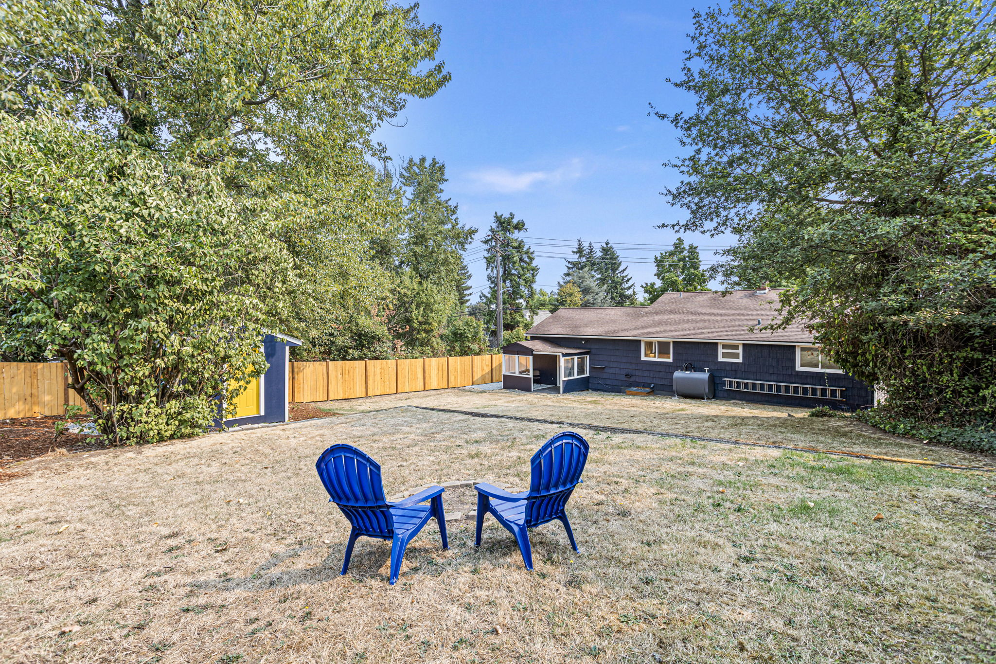 The upper terrace forms a natural gathering space, centered around a fire pit and surrounded by mature trees and dappled shade—a peaceful perch for outdoor connection.