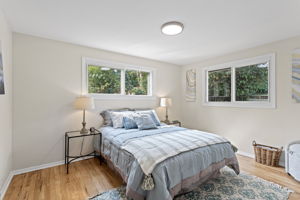 The south bedroom offers extra space and all-day light from its sunny corner windows, plus refinished hardwoods, new lighting, and updated closet doors.