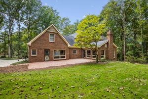 Brick exterior featuring a spacious brick patio, multi-gabled roofline, masonry chimney, and established wooded surroundings