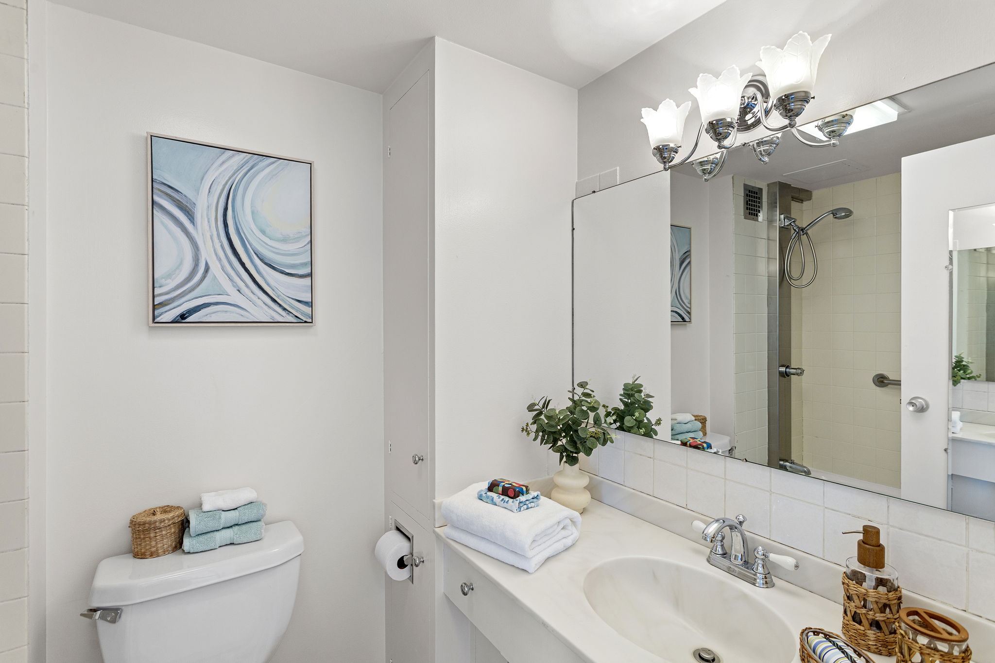 The bathroom is clean and bright, with a long vanity, generous mirror, and a classic tiled shower surround.