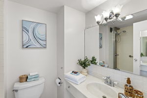 The bathroom is clean and bright, with a long vanity, generous mirror, and a classic tiled shower surround.