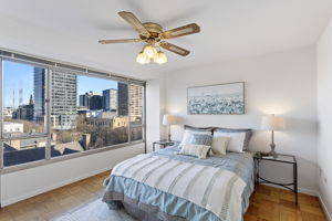 The bedroom keeps the same bright, open feel with expansive windows, a generous mirrored closet that amplifies the space, and a window A/C unit for warm days.