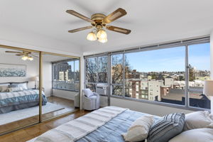 The bedroom keeps the same bright, open feel with expansive windows, a generous mirrored closet that amplifies the space, and a window A/C unit for warm days.