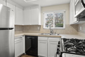 Kitchen with included refrigerator, gas range/oven, microwave, diswasher, tile counters, and window looking out to private fenced front yard