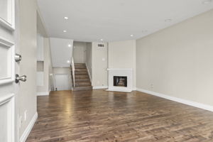 View from front door into unit's living room with gas fireplace. Kitchen & dining area to the left. Half-flight of stairs to mid-level with BRs 2 & 3 and a full hall bath. To left of visible stairs is half-flight of stairs down to 2 car garage.