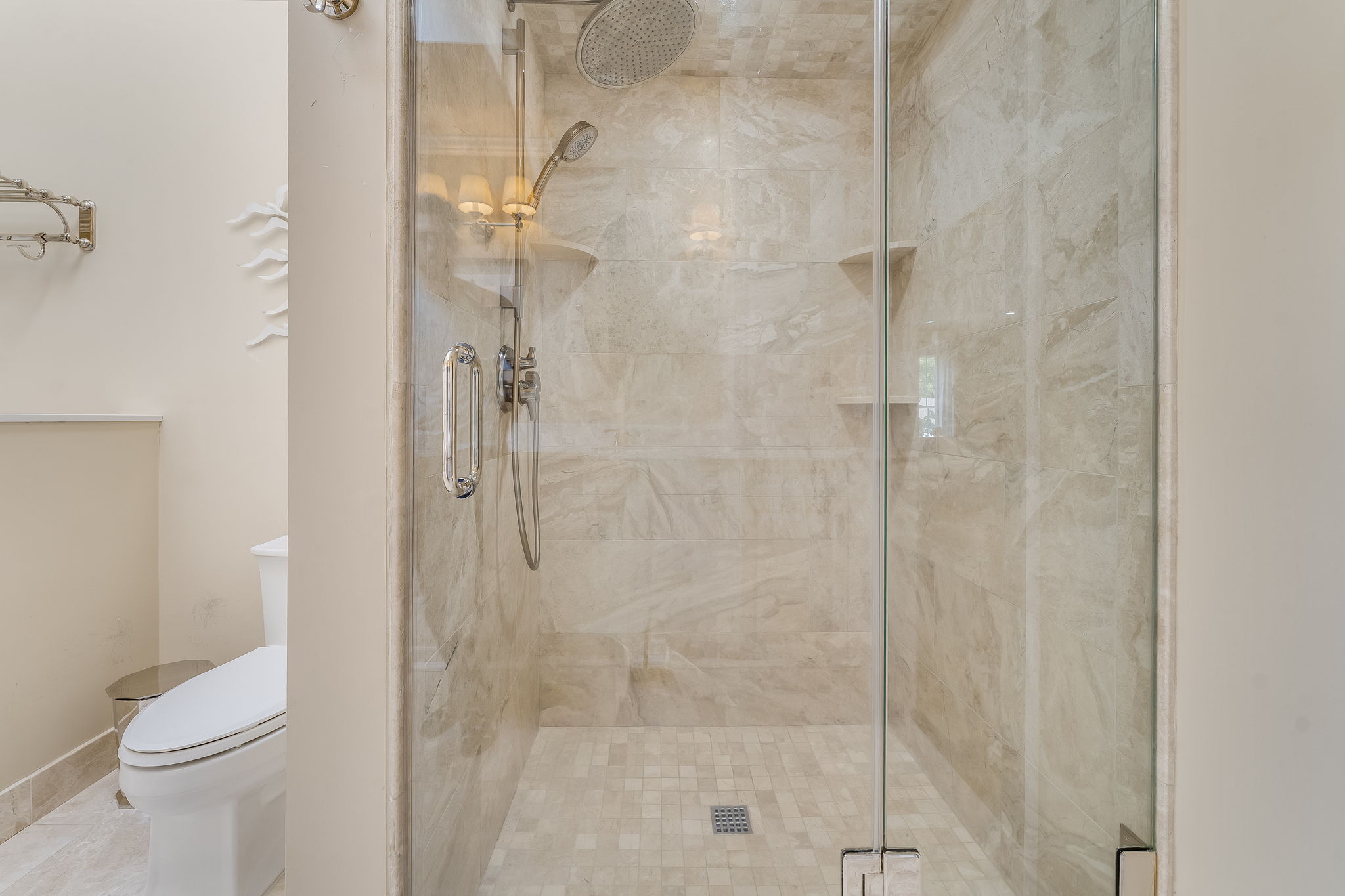 PRIMARY BATH European Shower in Travertine Tile Surround, Product Shelves, Frameless Door, Rain Shower Head + Hand-held Wand, Heated Towel Rack