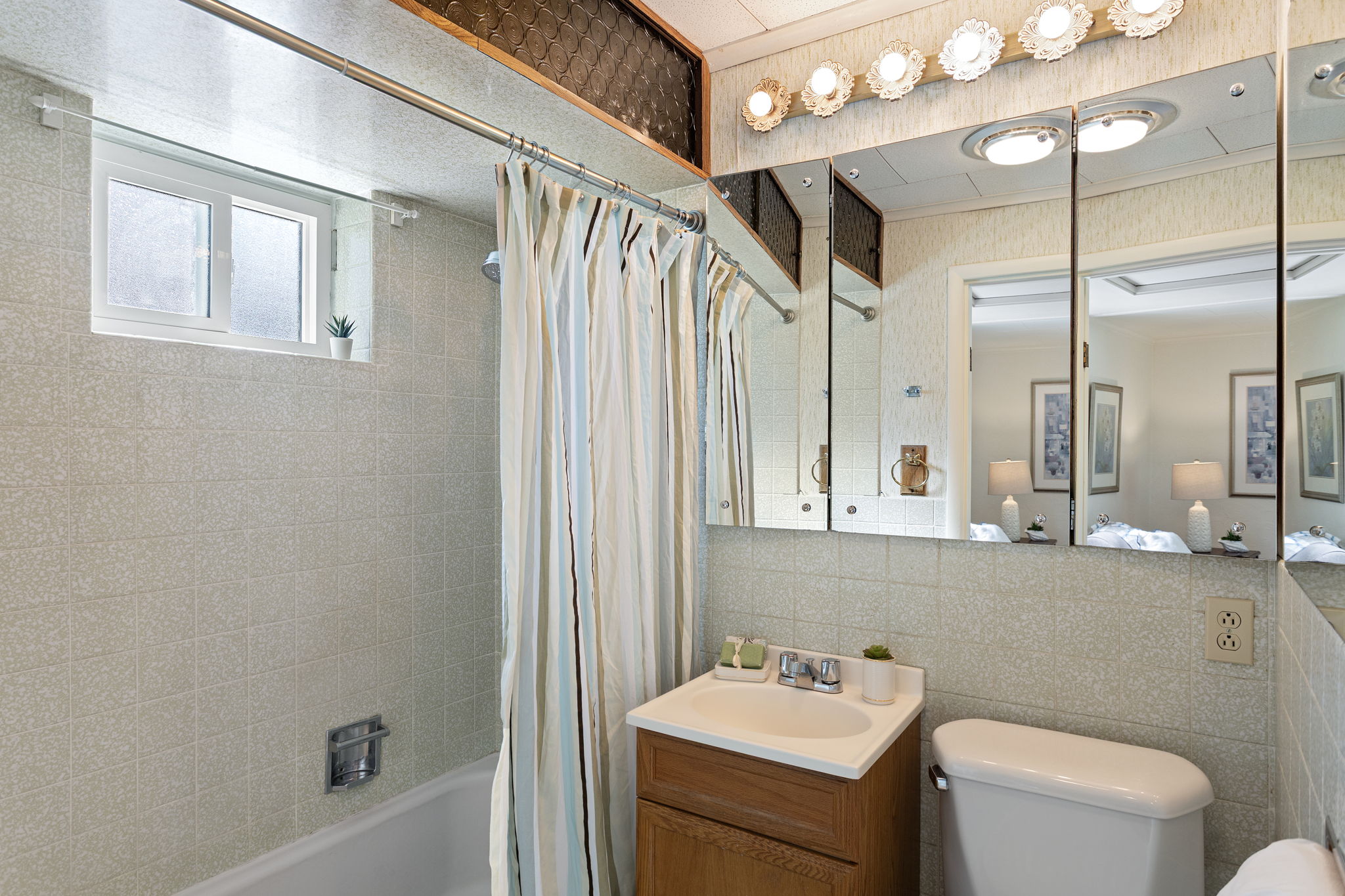 Full bath with tub/shower, mirrored storage, and natural light—simple and functional, with vintage charm.