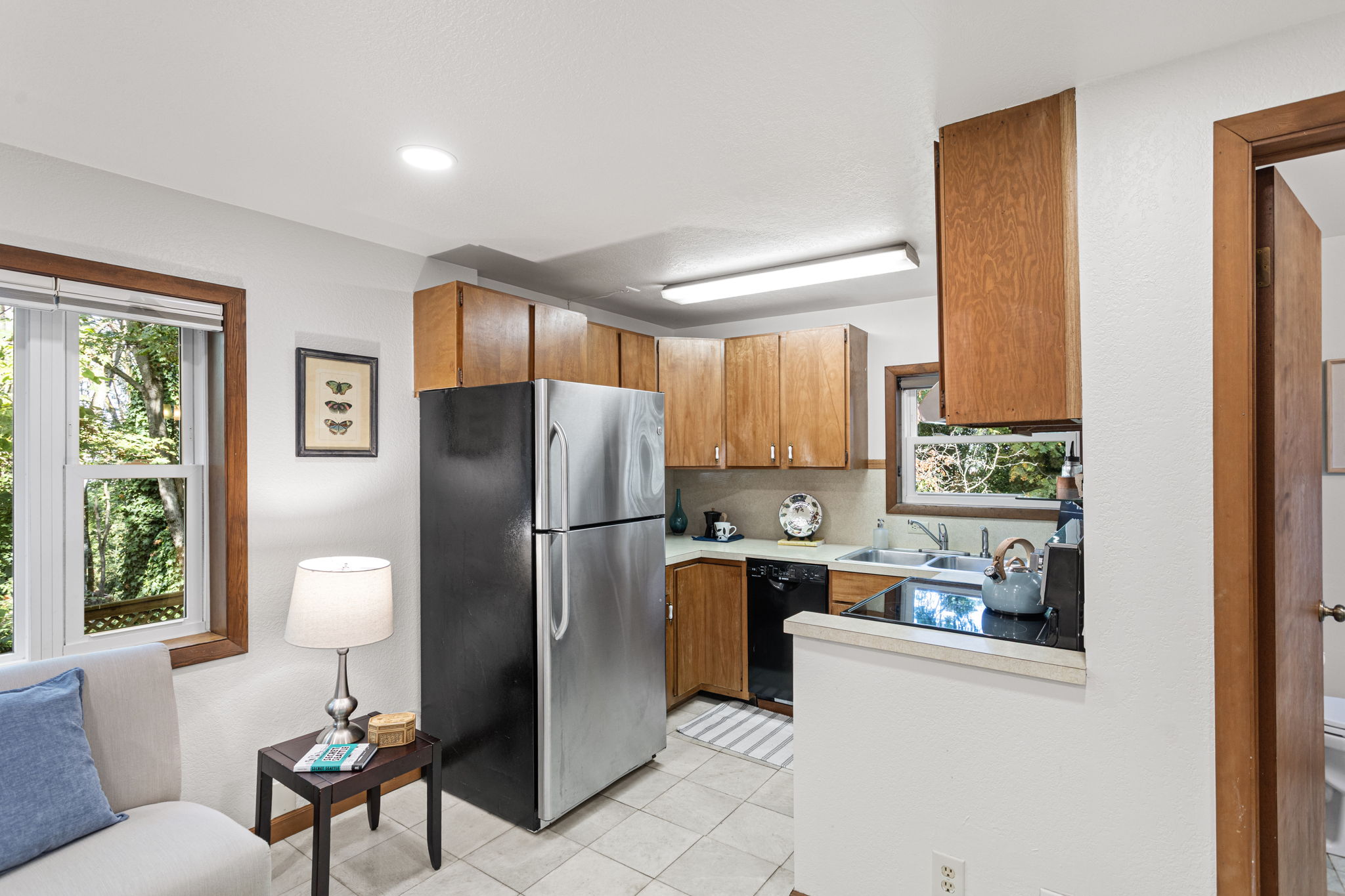 The kitchen offers classic wood cabinetry, granite-look Formica counters, and a full suite of appliances. Durable tile underfoot and a window above the sink keep it light and functional.