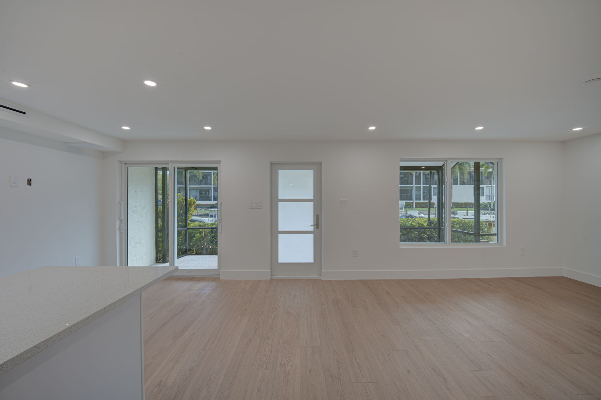 Empty primary living space featuring seamless wide-plank luxury vinyl plank (LVP) flooring, smooth finish ceilings, and impact-resistant sliding glass doors