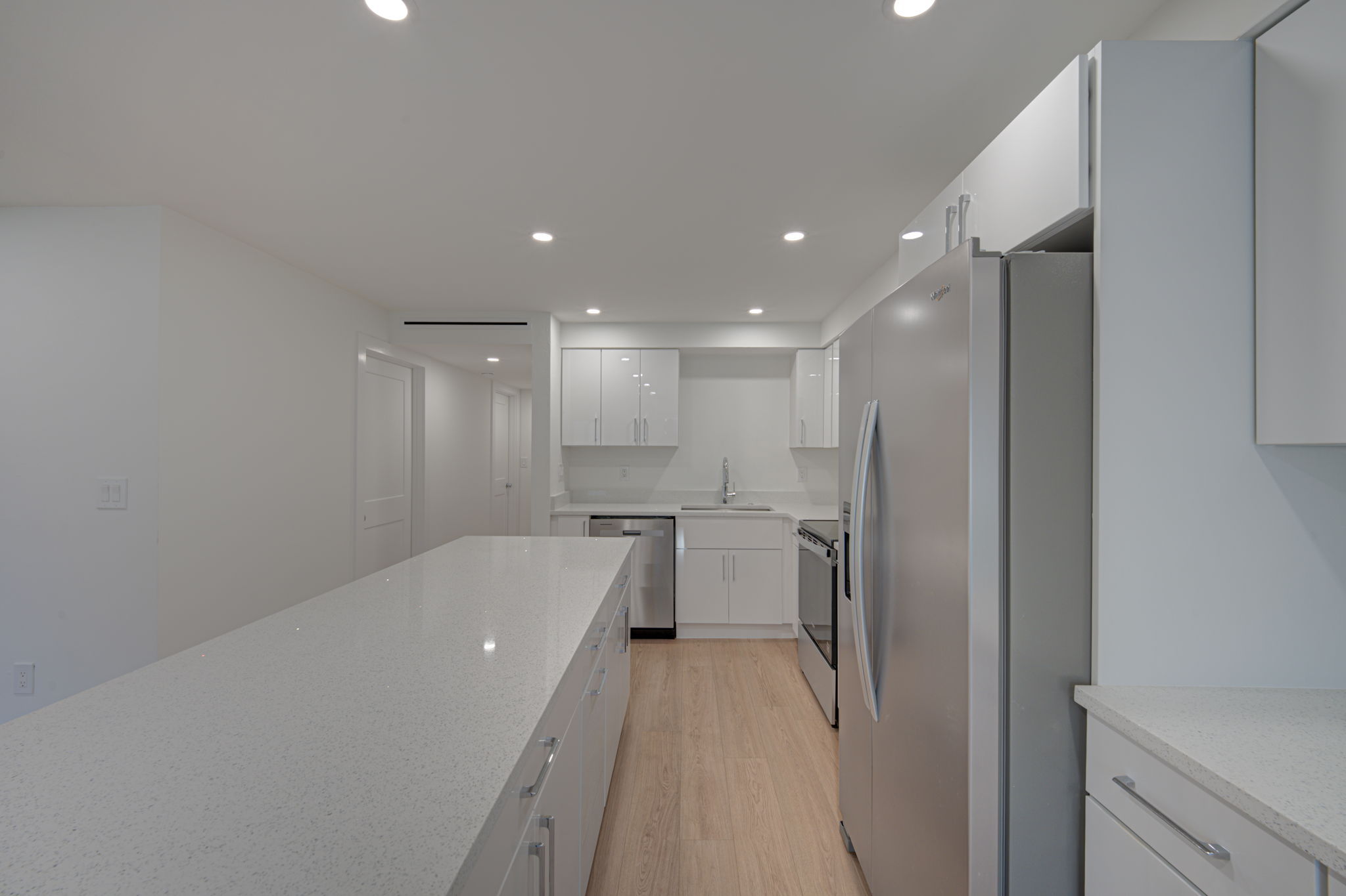 Alternate kitchen angle highlighting the stainless steel refrigerator, built-in pantry space, and structural sightlines into the hallway