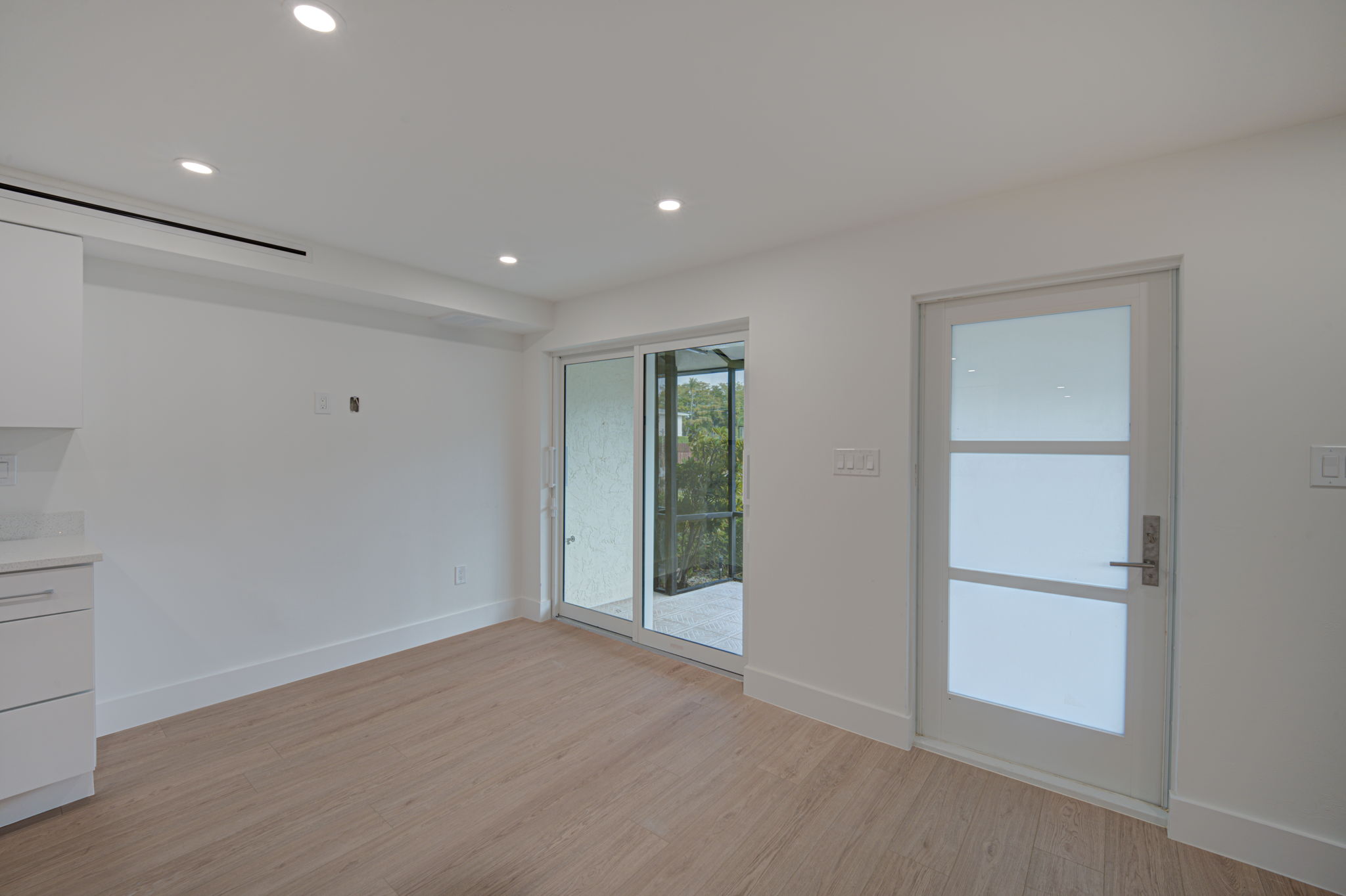 Primary bedroom suite featuring continuous LVP flooring, flush-mount lighting, and private impact-glass slider access to the waterfront lanai.