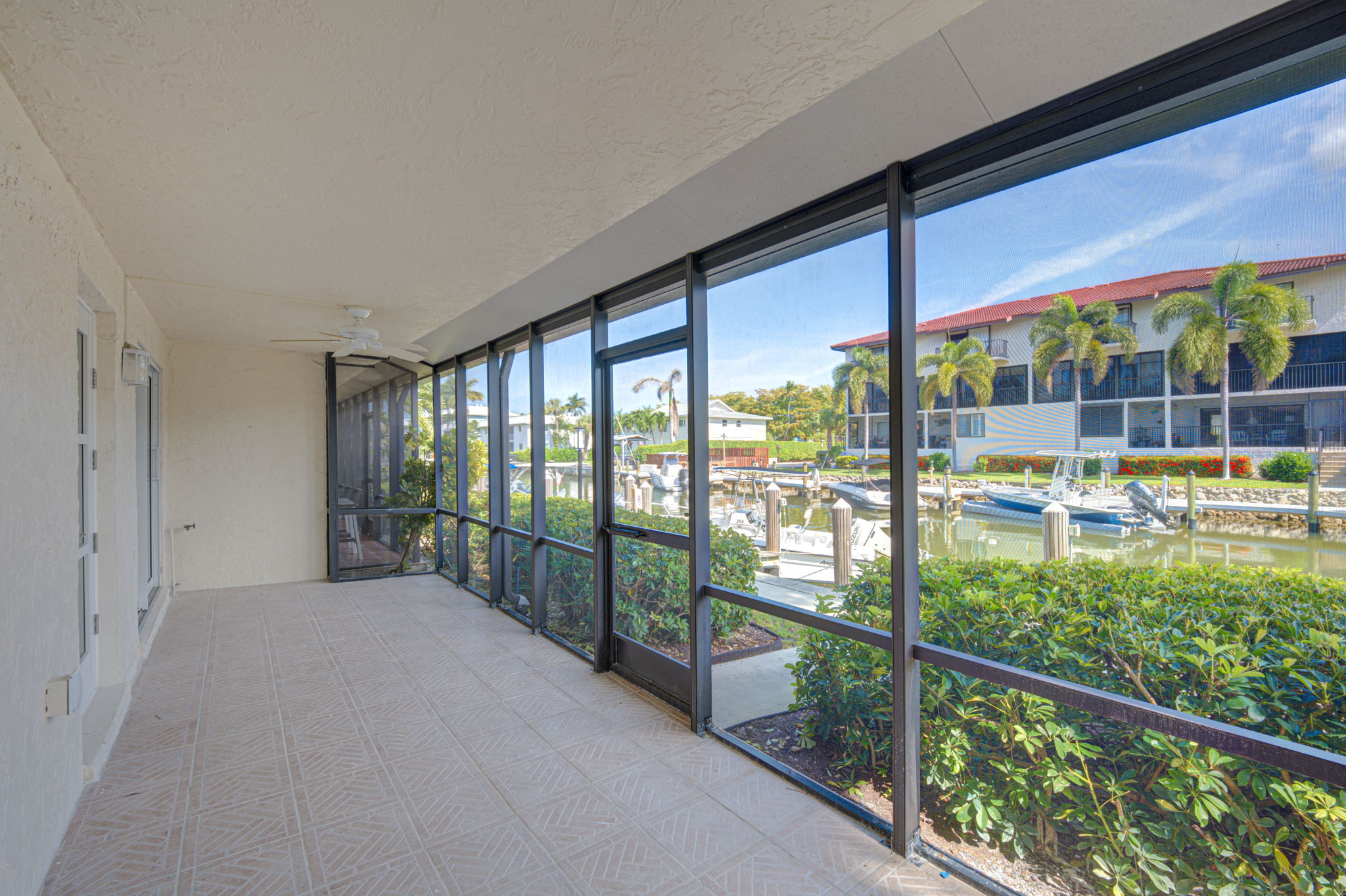 Expansive screened-in lanai with tile flooring, offering a protected outdoor living space with direct views of the canal and boat slips.