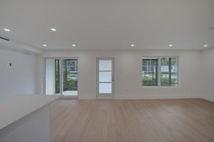 Empty primary living space featuring seamless wide-plank luxury vinyl plank (LVP) flooring, smooth finish ceilings, and impact-resistant sliding glass doors