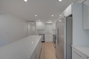 Alternate kitchen angle highlighting the stainless steel refrigerator, built-in pantry space, and structural sightlines into the hallway