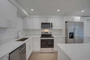 Close-up of the kitchen workspace detailing the deep stainless steel undermount sink, commercial-style pull-down faucet, and polished quartz surfaces.