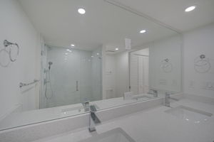 Upgraded bathroom vanity area featuring a double-sink quartz countertop, shaker cabinetry, and an oversized framed mirror