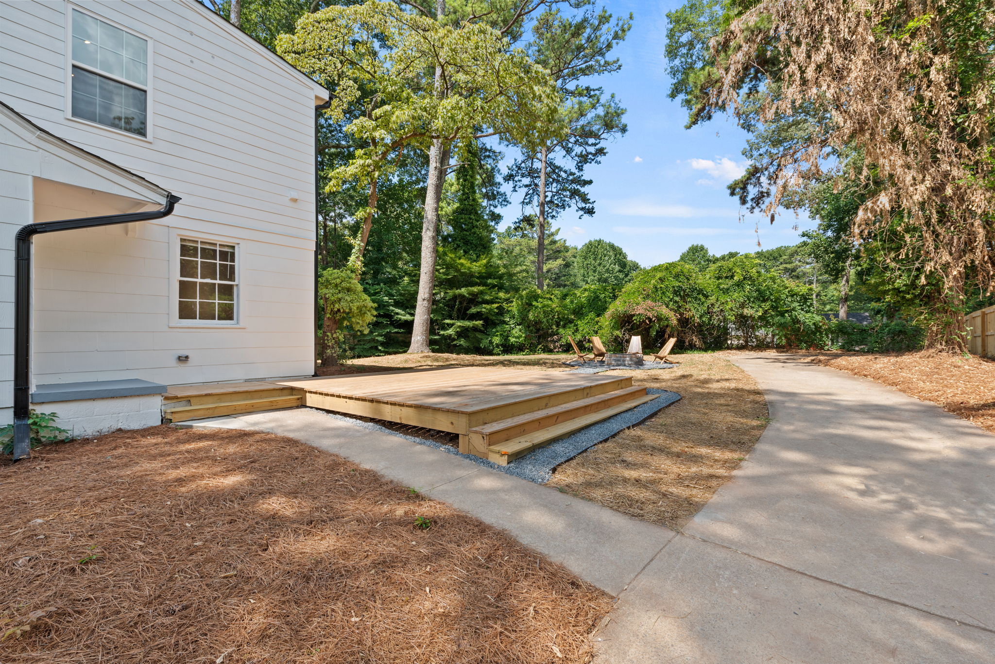 Backyard - Extending beyond the gate to the back of the property, the driveway leads to a backyard oasis with a big deck and fire pit. A private paved landing area provides versatility for parking cars, your dream shed, or creating an additional outdoor entertainment space.