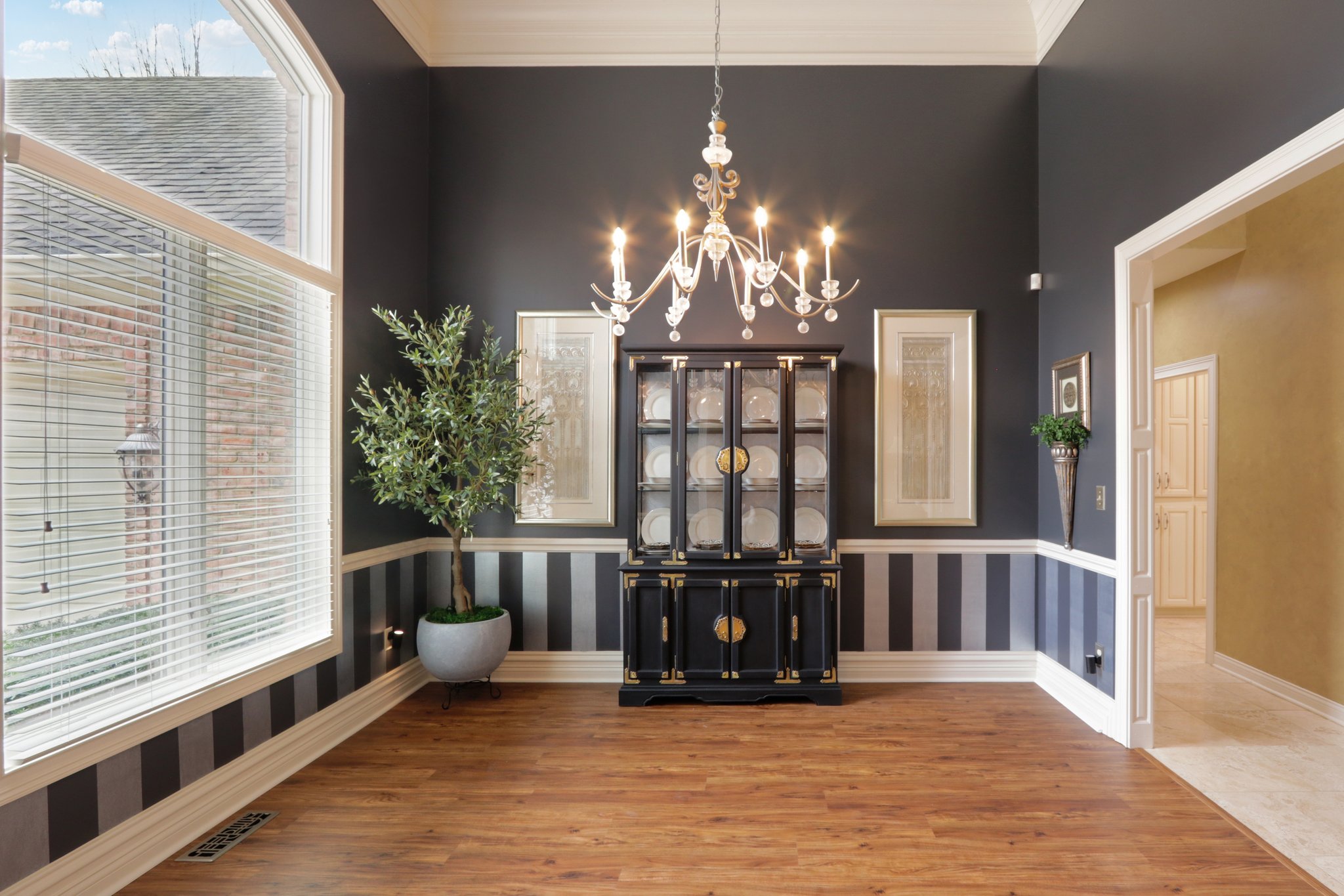 Dining room with soaring ceiling and dramatic chandelier, large windows opens to foyer and hallway to gourmet kitchen