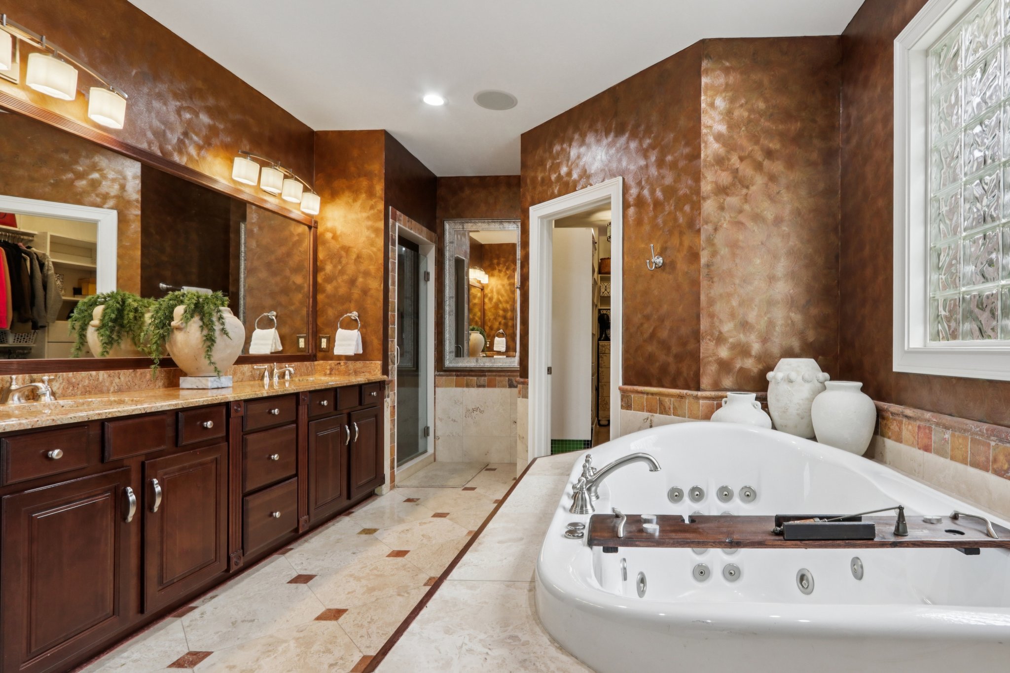 Luxurious primary bathroom suite featuring deep whirlpool bathtub, large vanity with double sinks, walk-in closet, separate linen closet, tiled walk in shower and private water closet