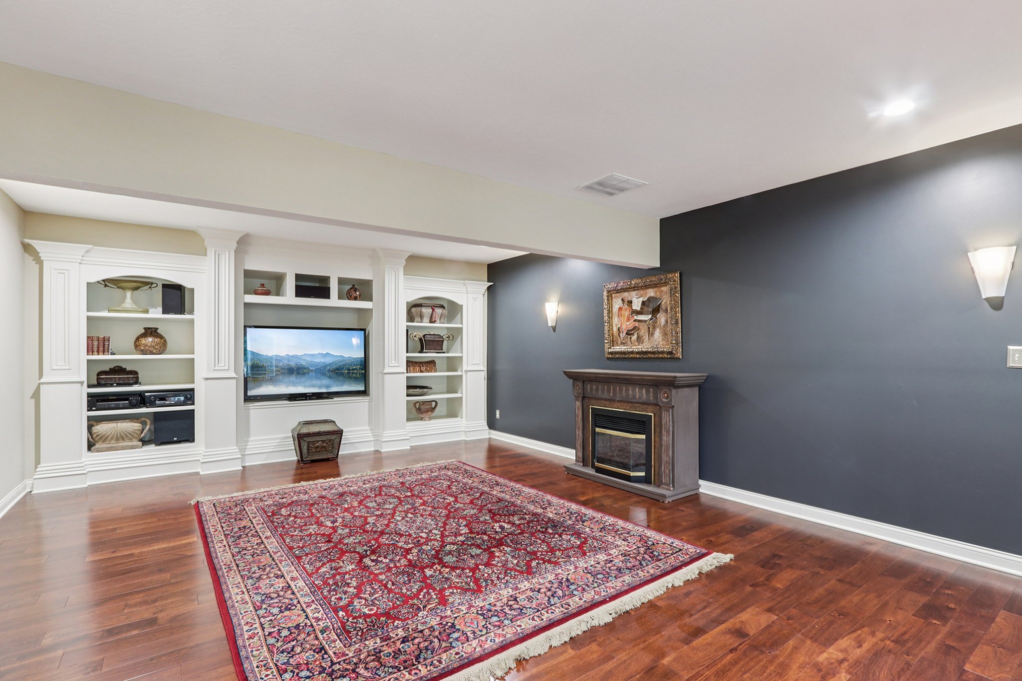 Media room with built-in cabinets, decorative sconce lighting and hardwood flooring