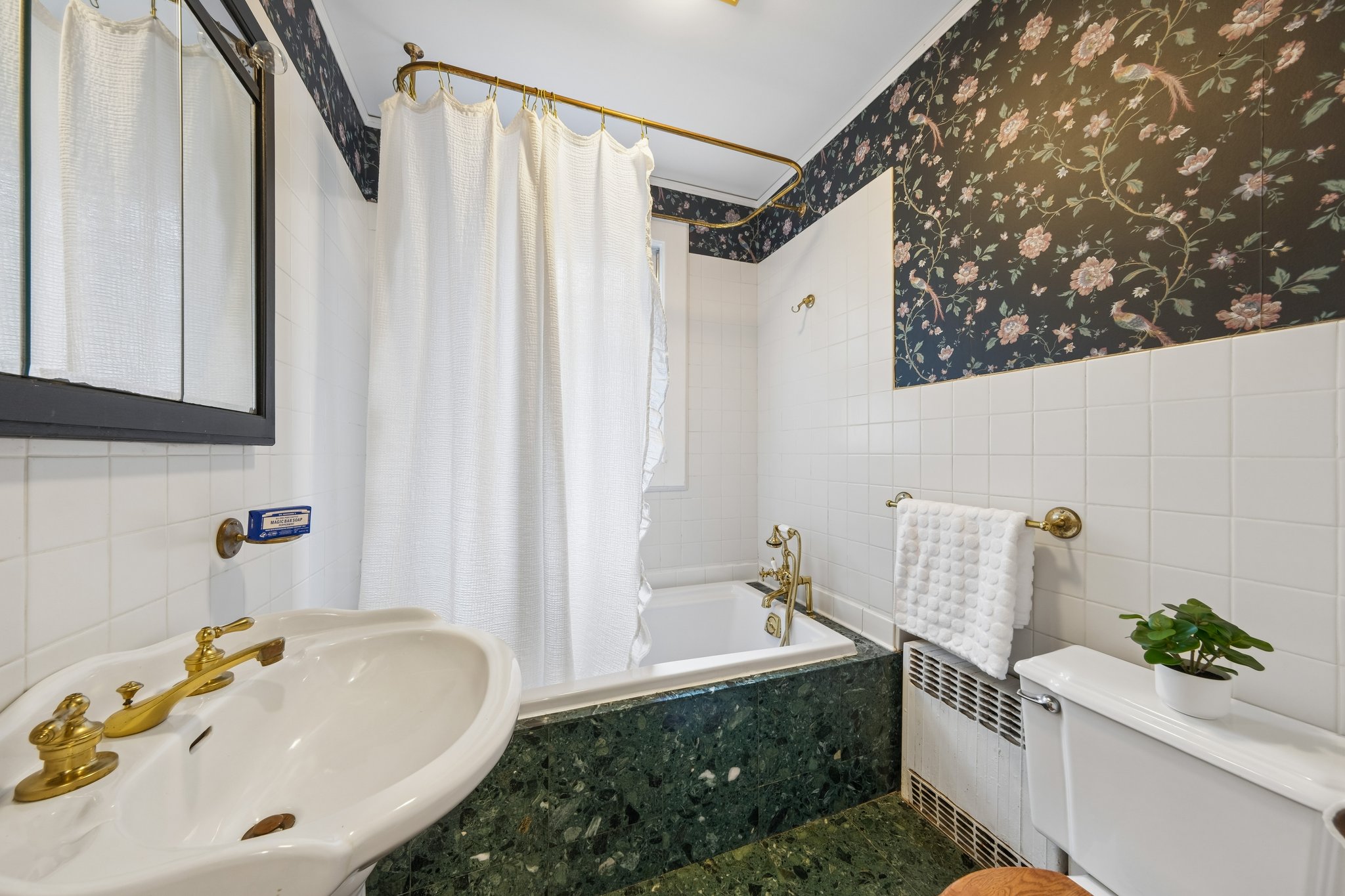 A FULL BATH, RIGHT WHERE IT HELPS. The first-floor bath adds flexibility for guests and everyday life, with floral wallpaper and warm metal details bringing charm to the practical.