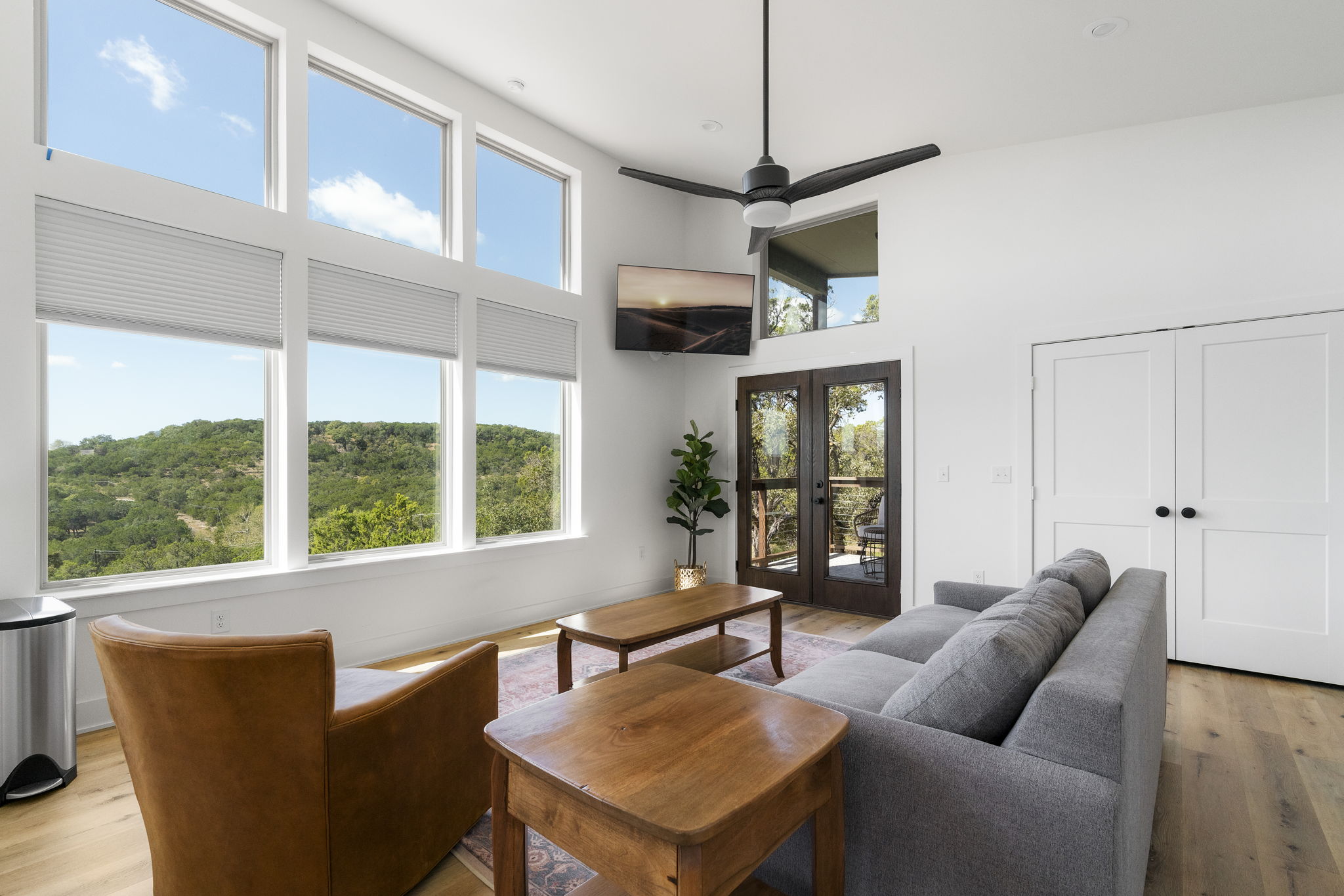 The living room of this fully furnished unit features breathtaking views of the Wimberley Valley through floor-to-ceiling windows, allowing for stunning natural light throughout the space.