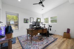 The secondary bedroom, shown here as an office but available with bedroom furnishings, boasts several large windows, white oak wood floors, and additional scenic views.