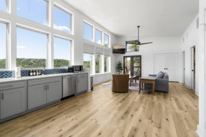 The kitchen and living room seamlessly flow together in an open layout, featuring floor-to-ceiling windows, white oak wood floors, and modern finishes throughout.