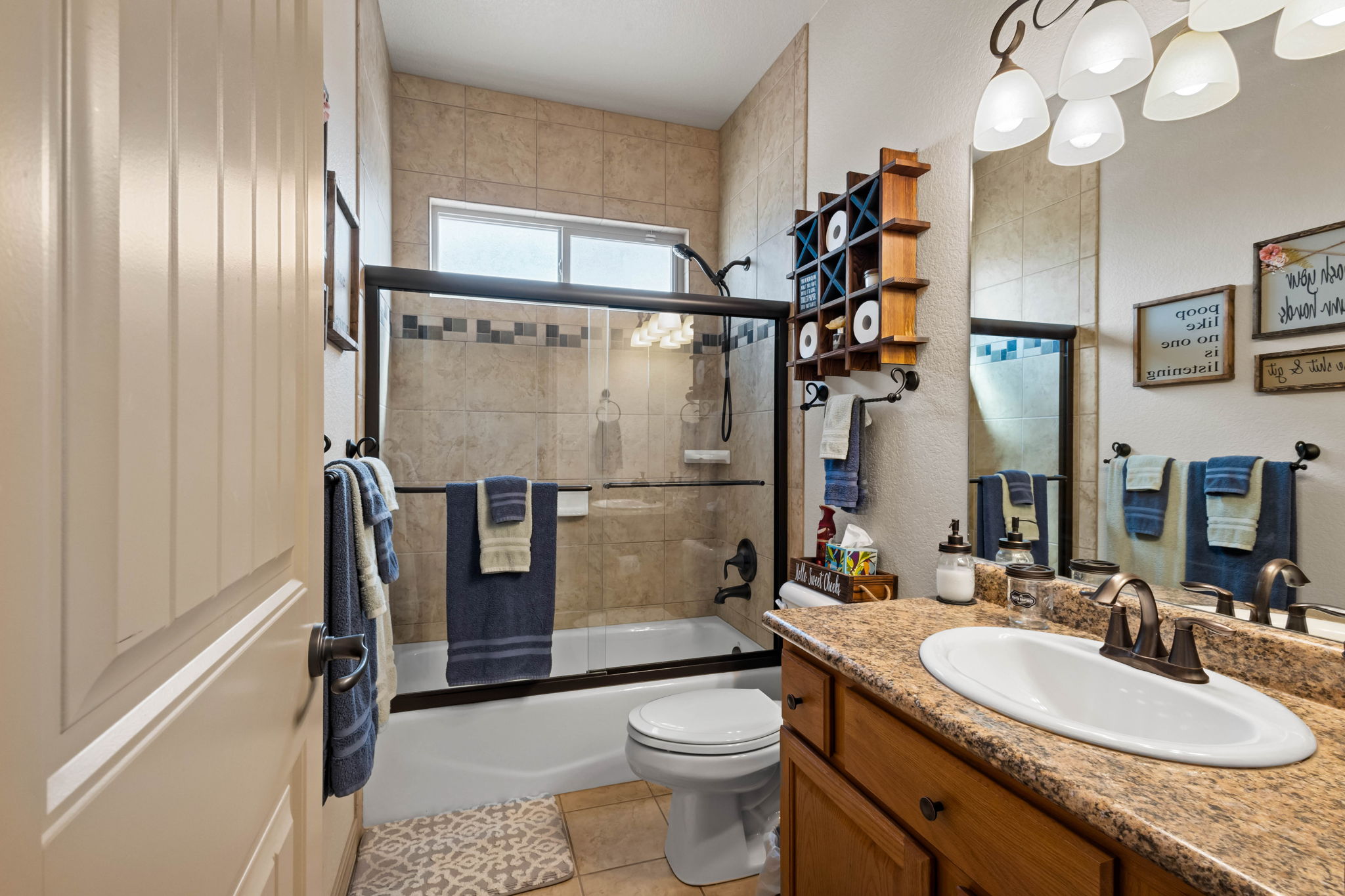 Full bathroom with tile flooring, large vanity, shower/tub combo with glass enclosure accented with tiles.