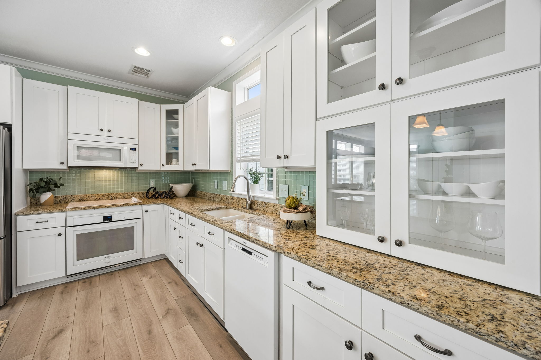 The kitchen continues with generous counter space, glass-front cabinetry, and clean white finishes ...