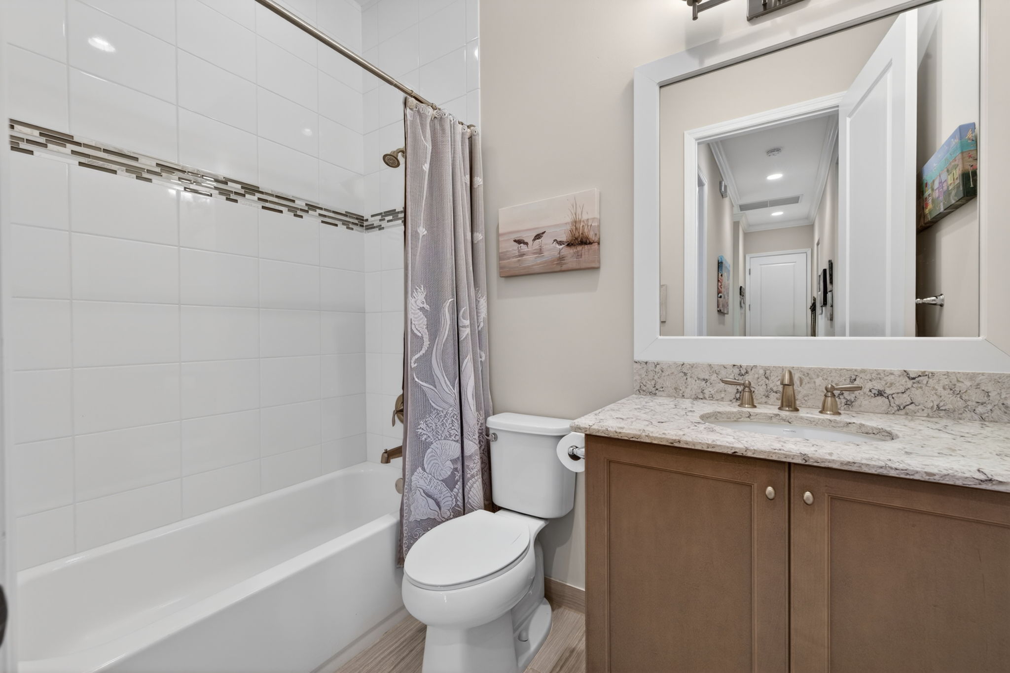 2nd full bath features floor to ceiling tile, wood framed mirror and continuous plank tile flooring.